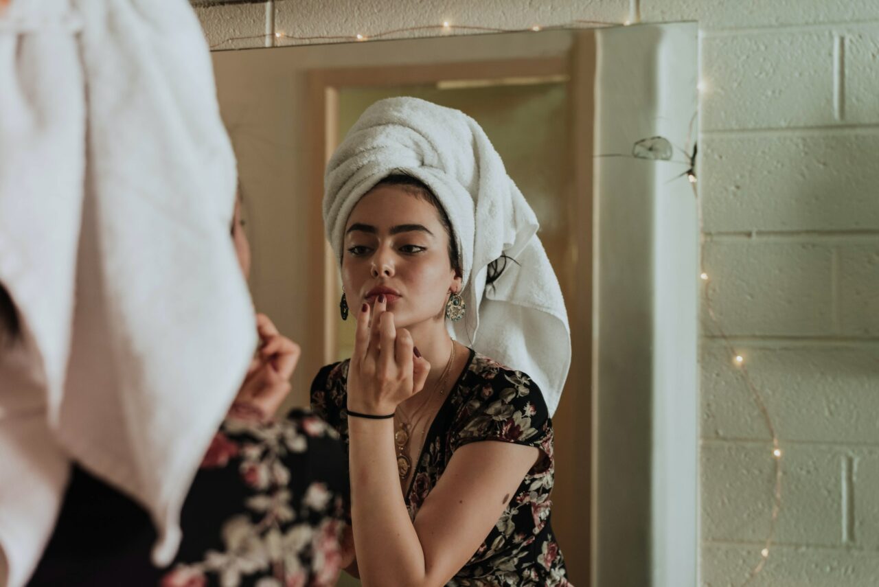 Girl with towel on her head putting makeup on in the mirror