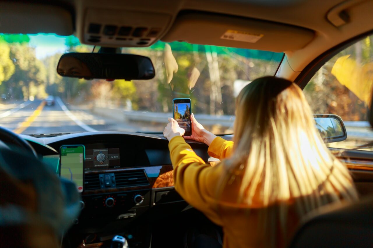 Passenger taking a photo through car window on a road trip