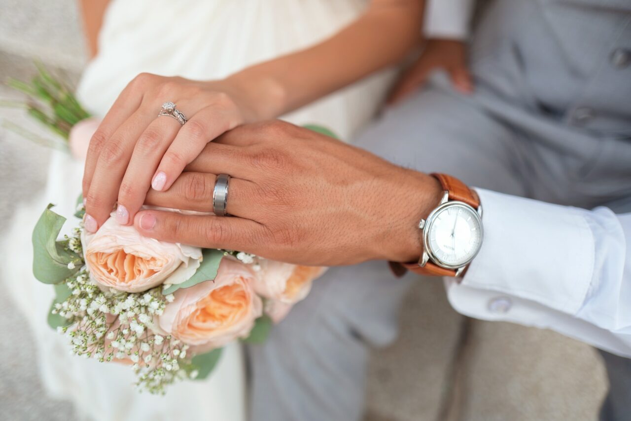 Married couple with wedding bands touching the bouquet