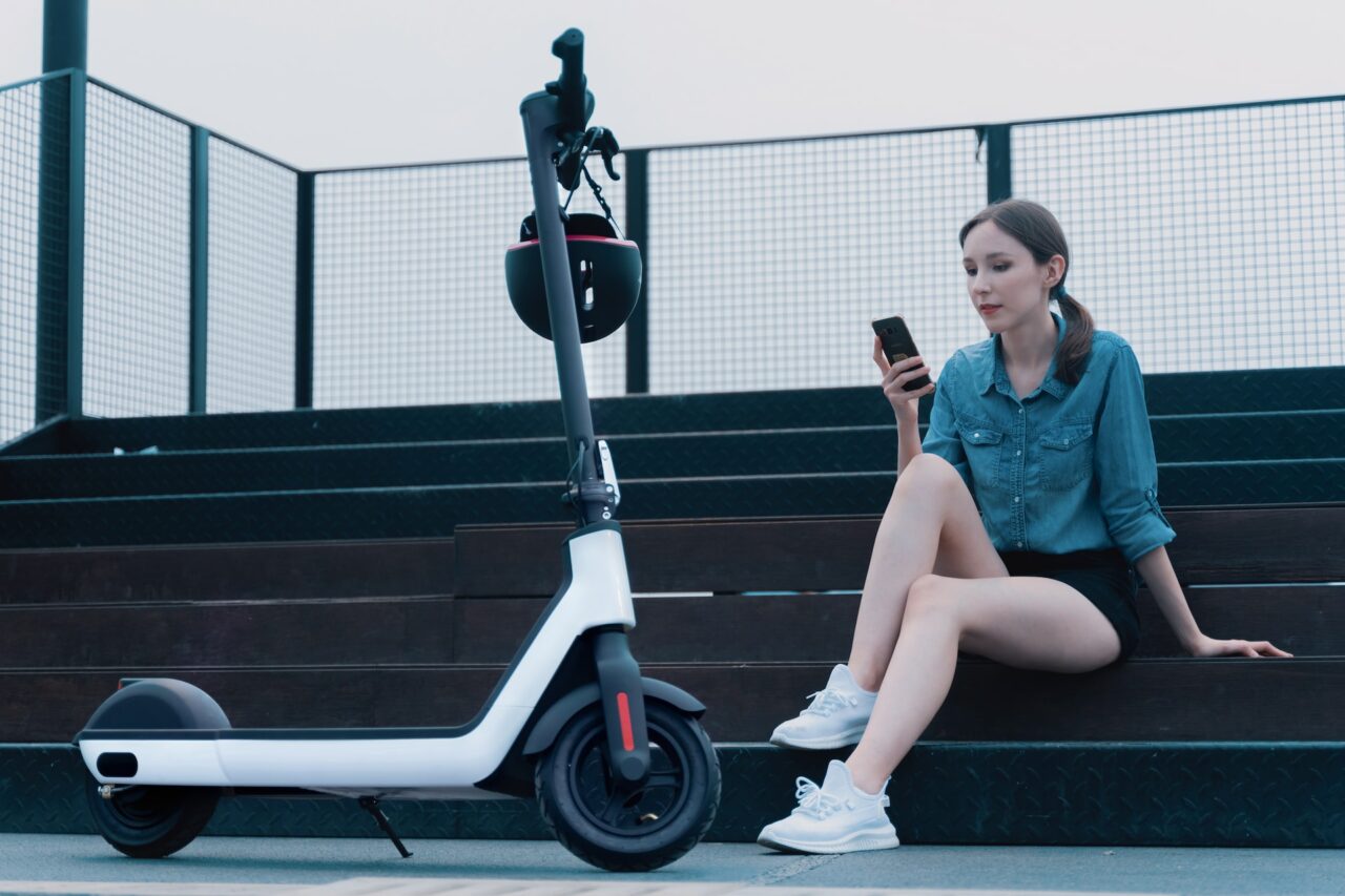 Girl on the phone, sitting next to an electric scooter