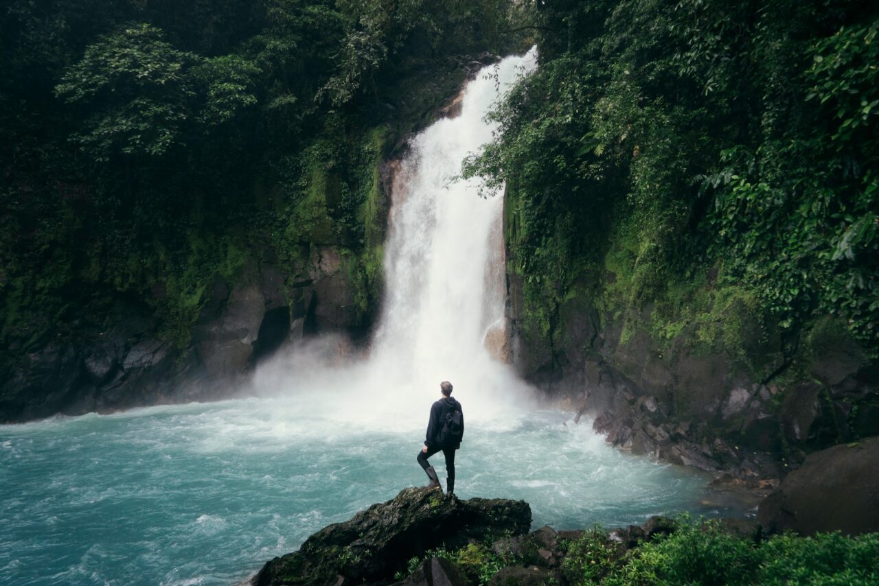Man standing on top of a rock next to a waterfall