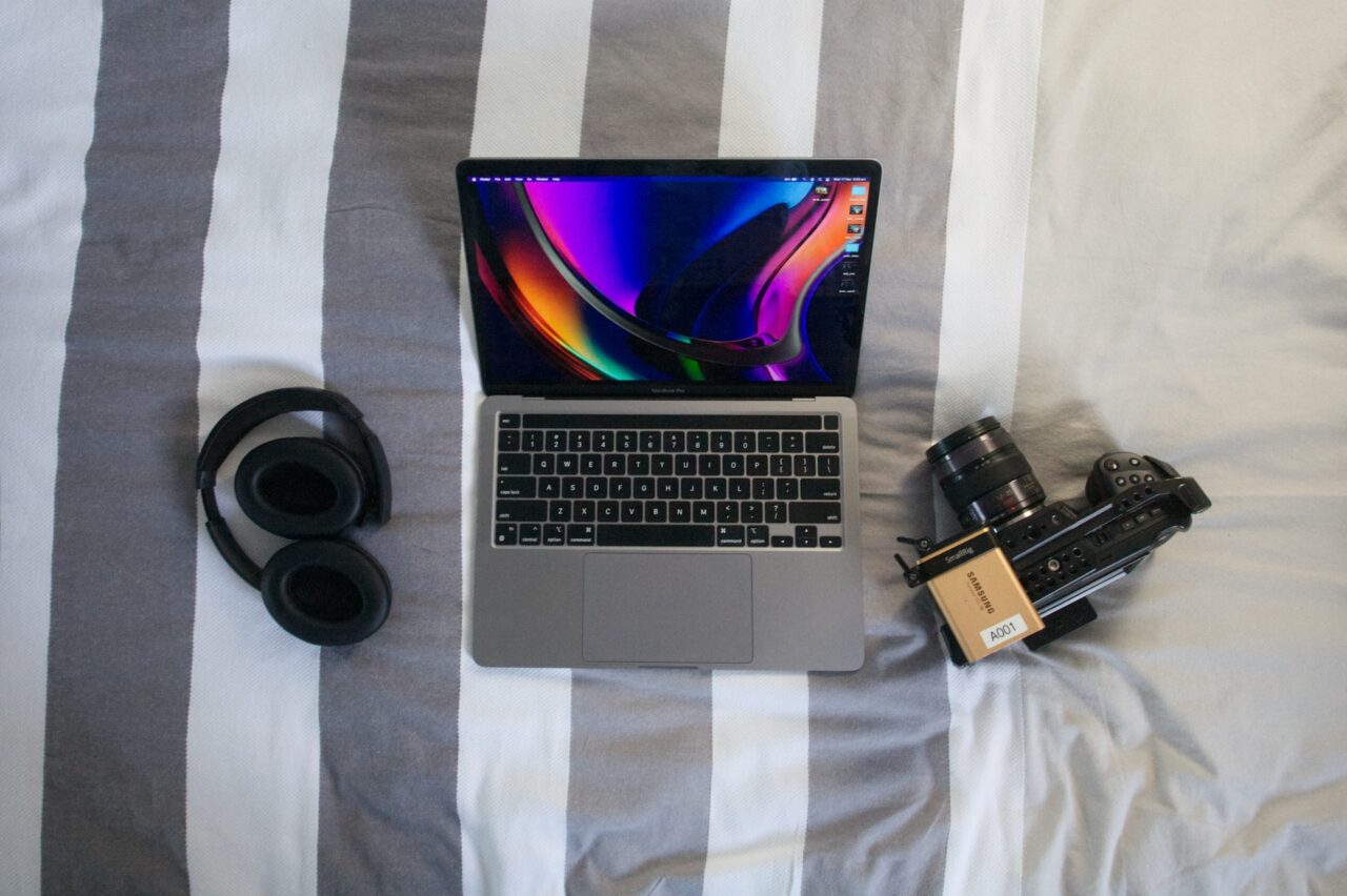 Laptop, camera and headphones on a bed