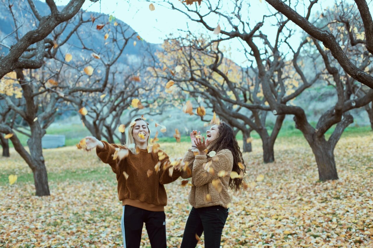 Two girls throwing leaves in the air in fall
