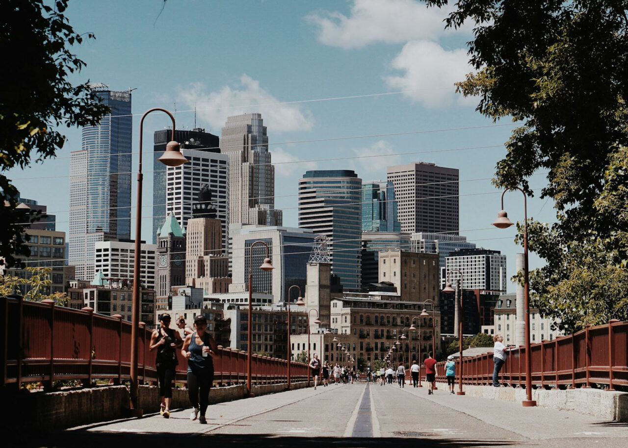 Runners running along a walkway in front of the Minneapolis skyline