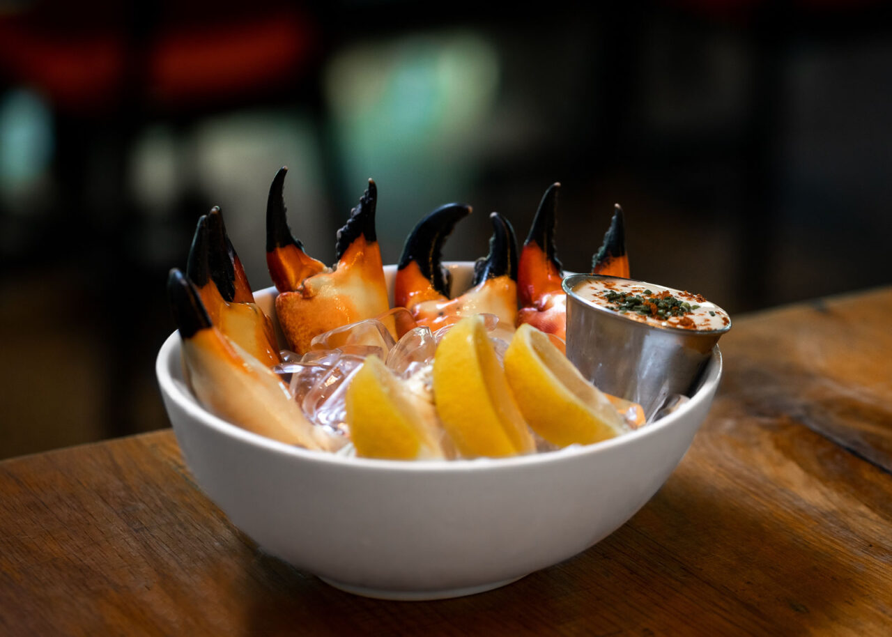 Stone crab claws in a white bowl with lemons and dip
