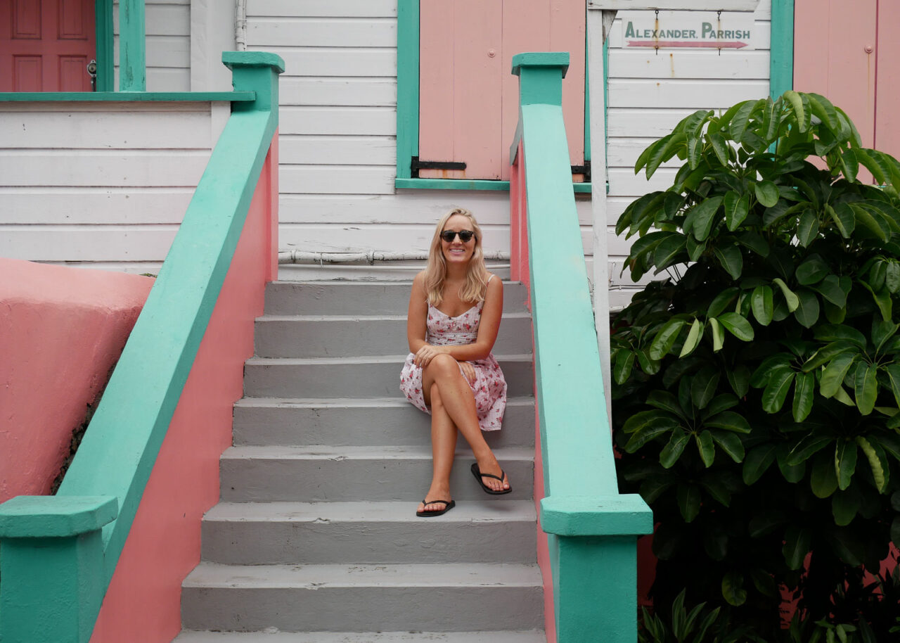 Solo female traveler sitting on a step in front of a colorful house in Antigua