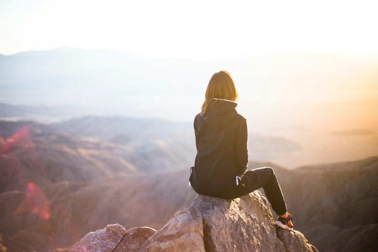 Woman wearing a jacket sitting on a rock looking out at the view