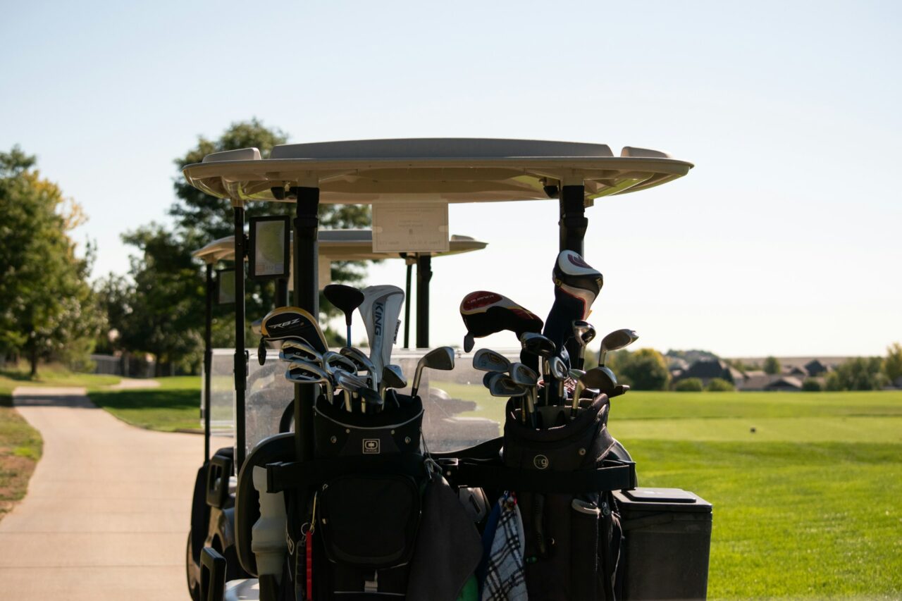 Golf buggy filled with clubs next to a golf course