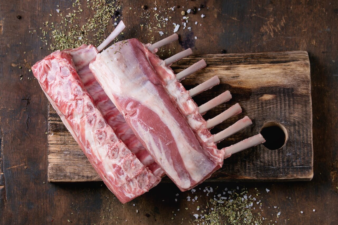 Rack of lamb on a wooden chopping board with salt and herbs