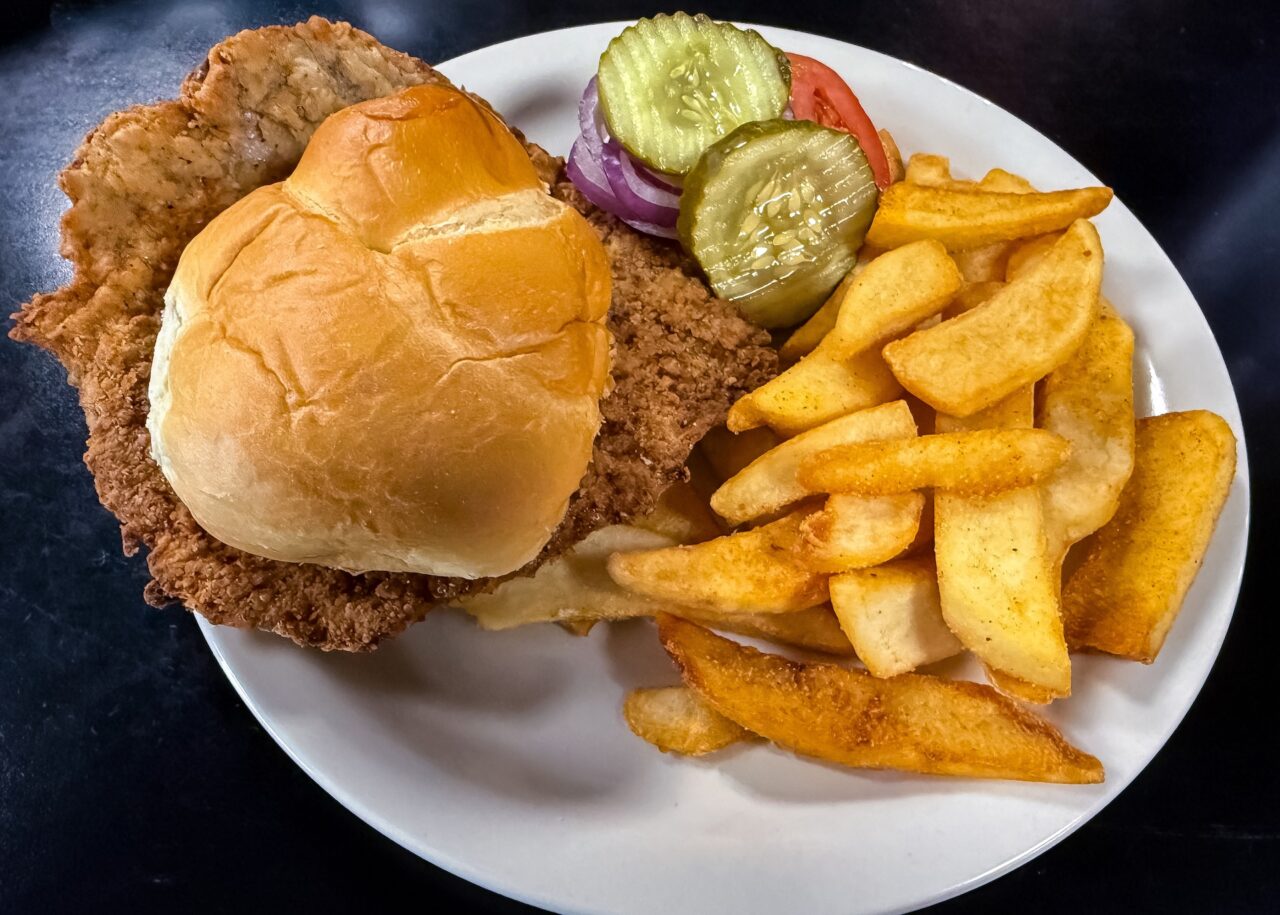 Breaded pork tenderloin sandwich on a white plate with fries