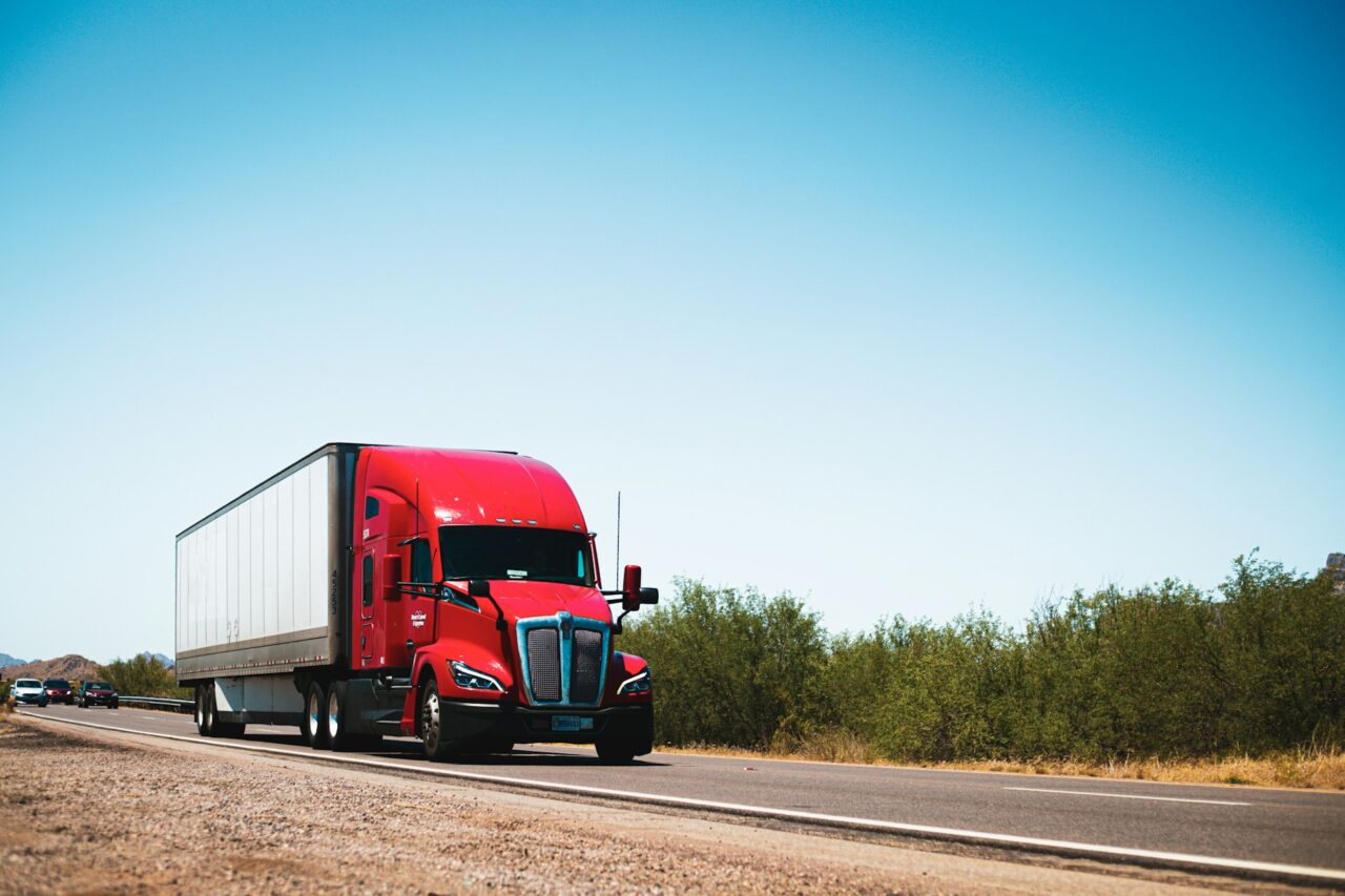 Red truck driving along an open road on a sunny day