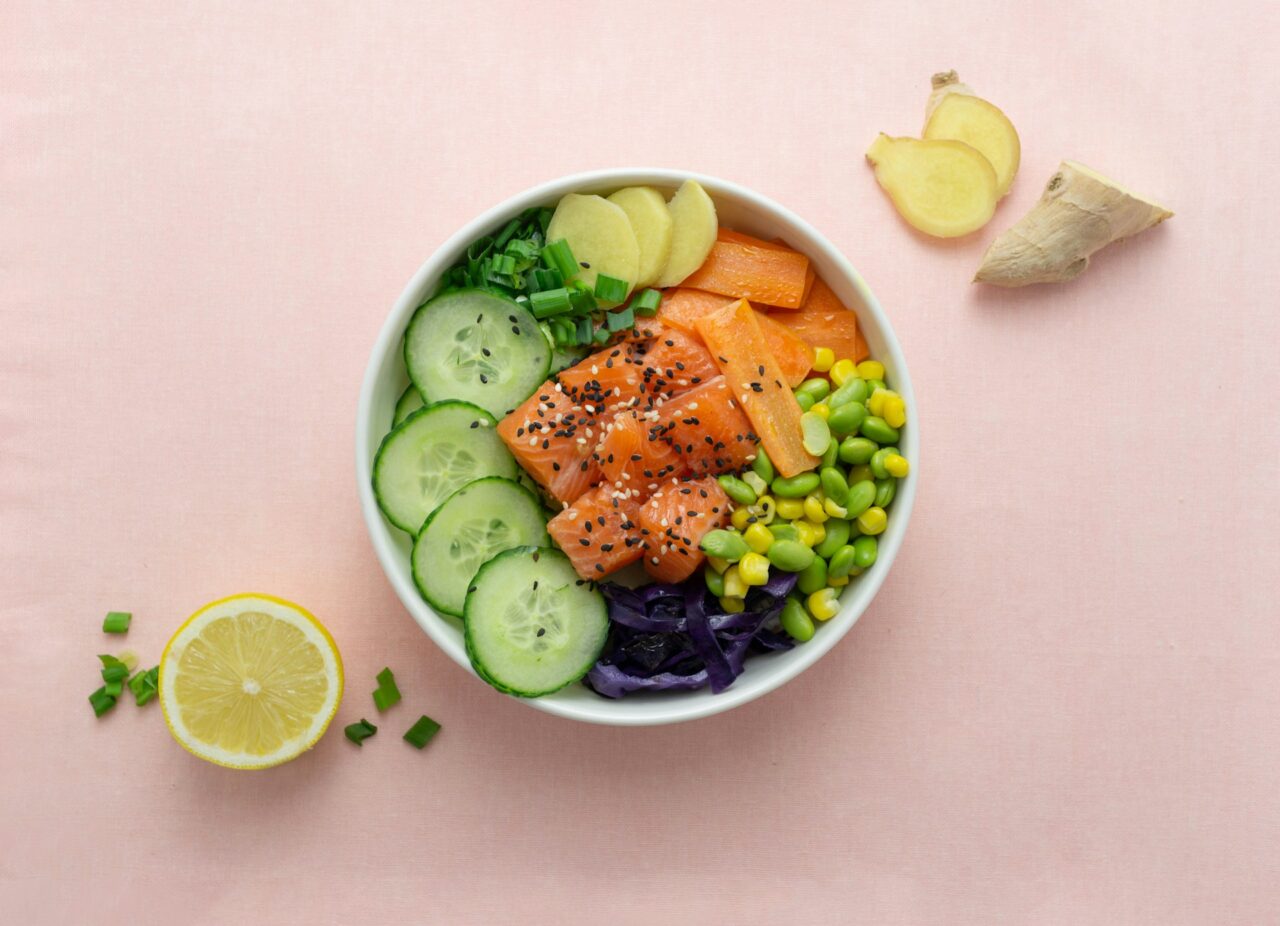 Salmon poke bowl with cucumbers and edamame on a pink background