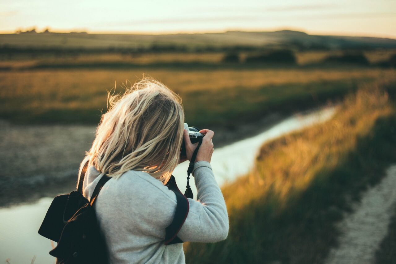 Woman holding a camera taking a photo of a field