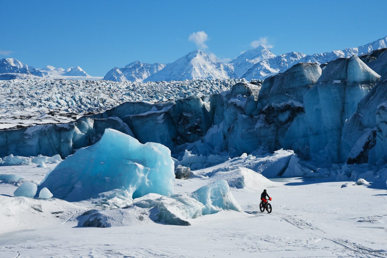 Man on bike riding across the snow at Kink Glacier