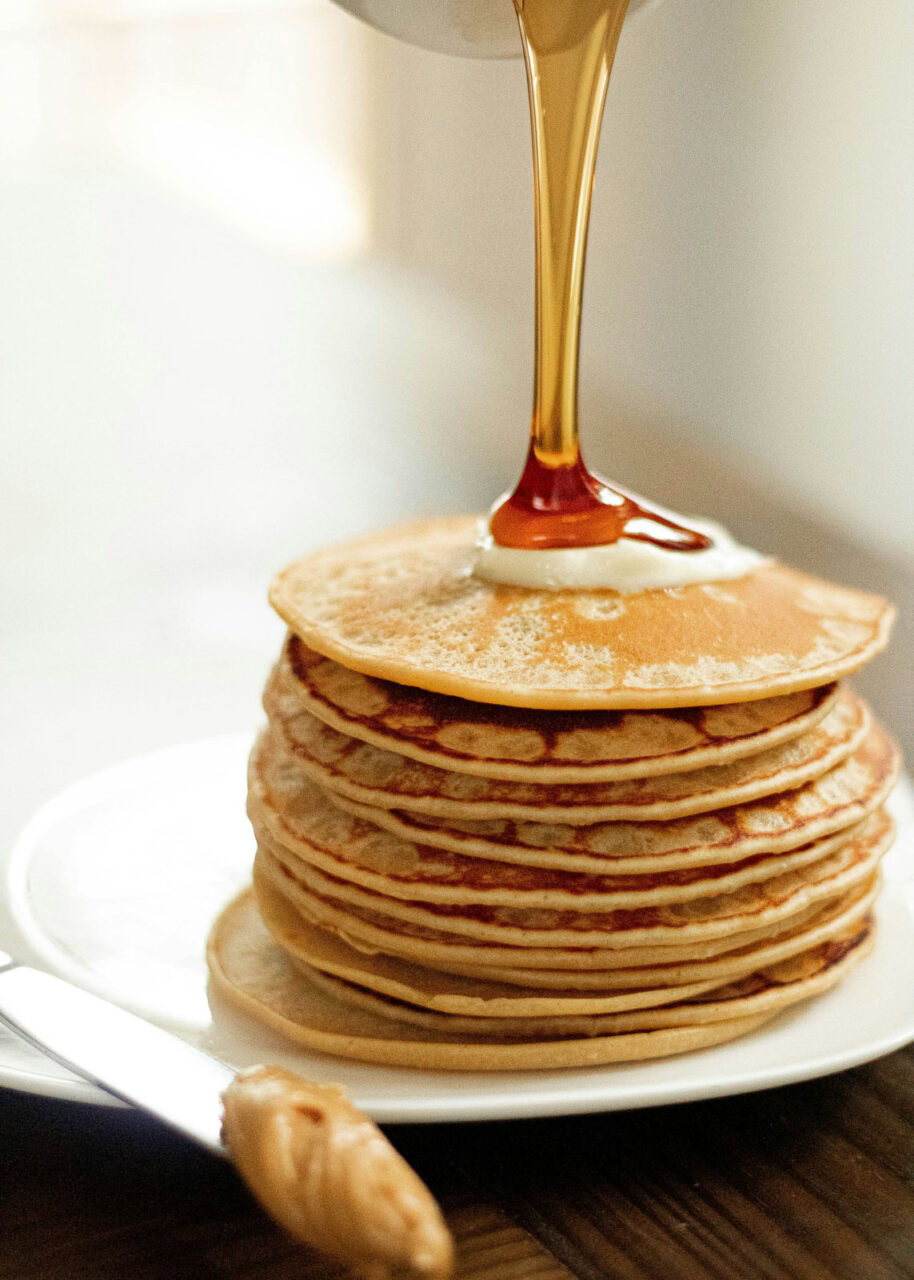 Maple syrup being poured on a stack of pancakes