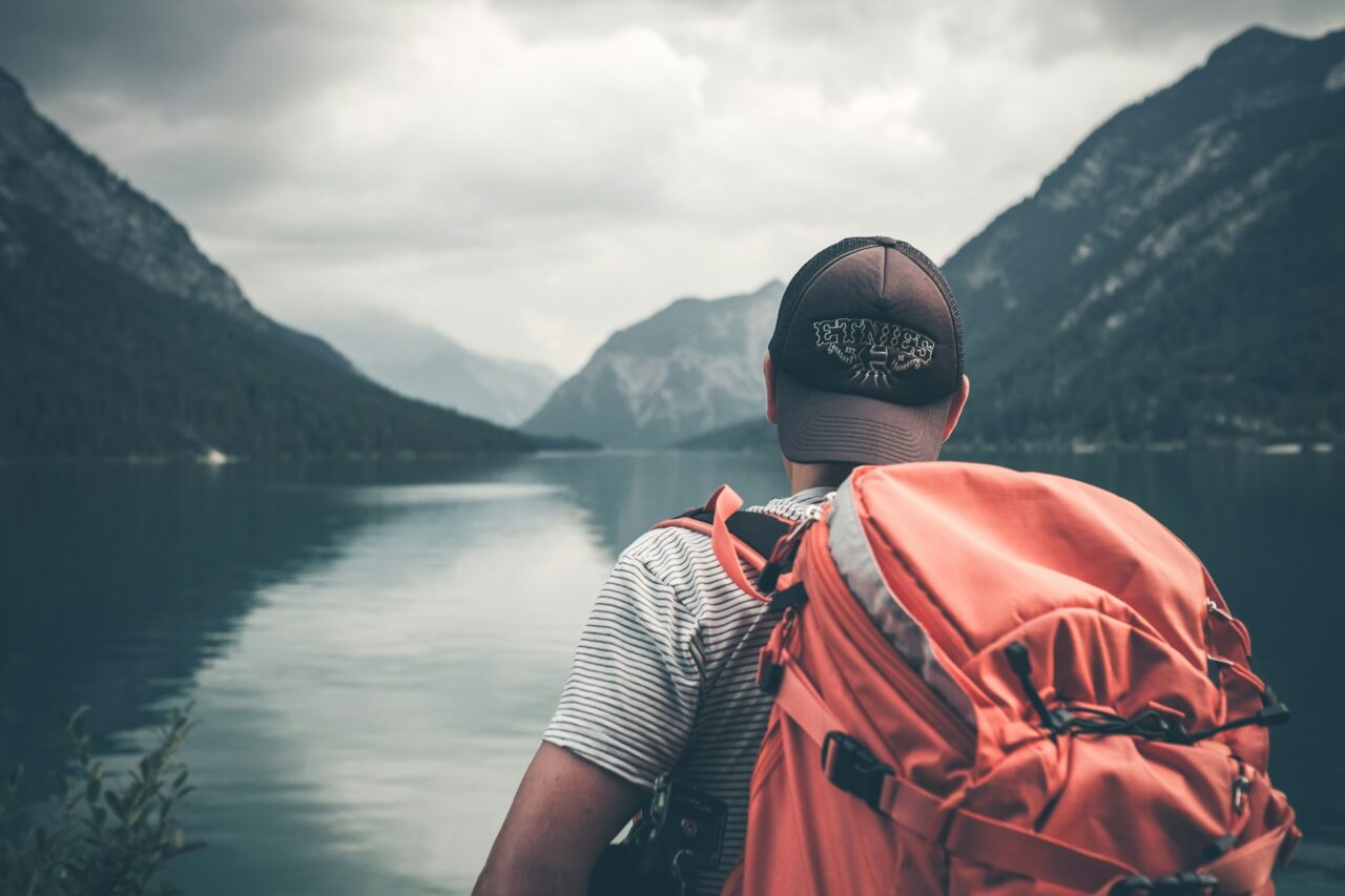 Man with red backpack next to a lake