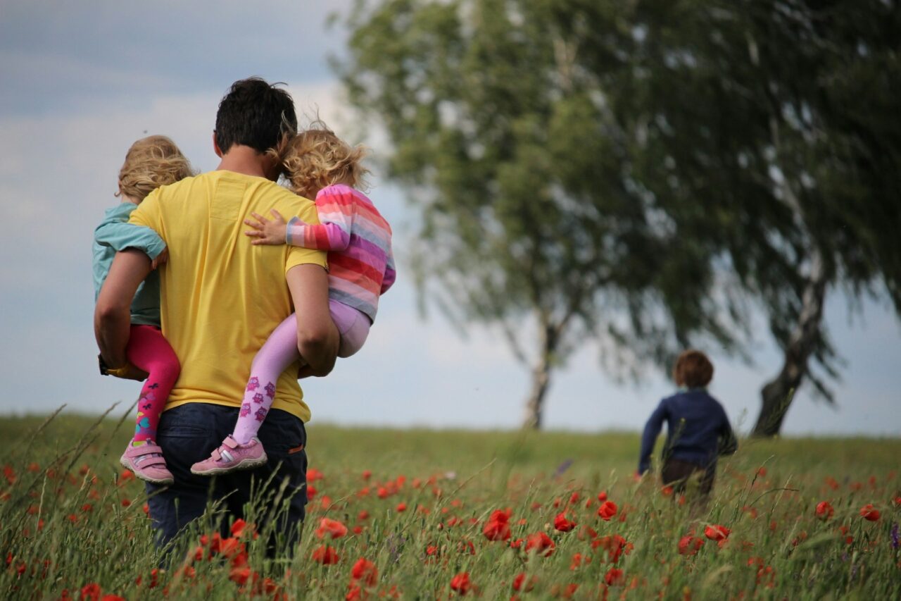 Man carrying two kids through a field