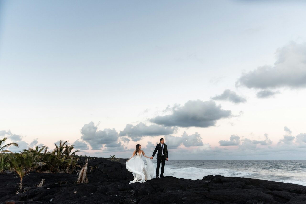 Bride and groom on black volcanic cliff in Hawaii