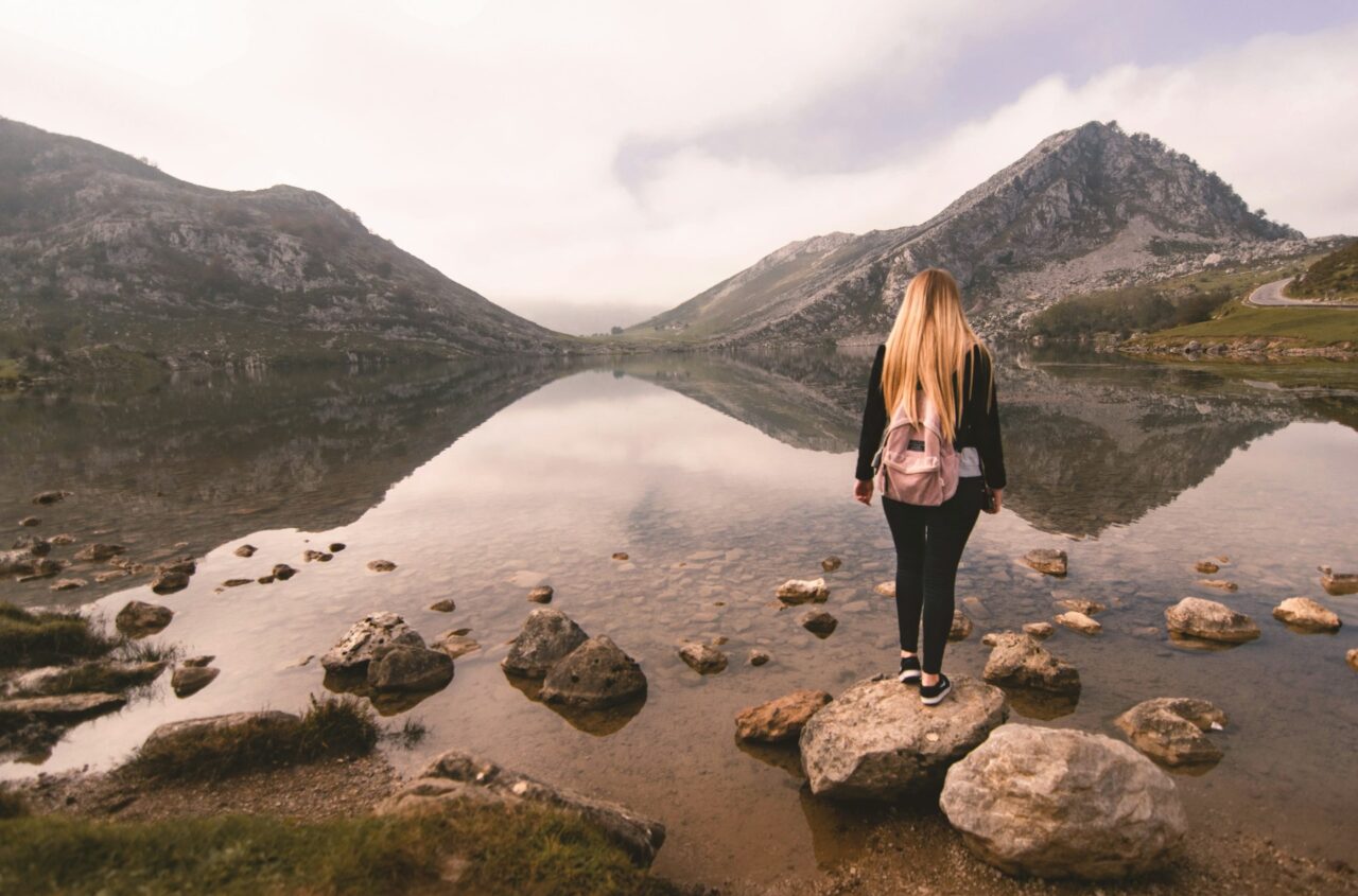 Female traveler standing on a rock looking out at a lake with mountains