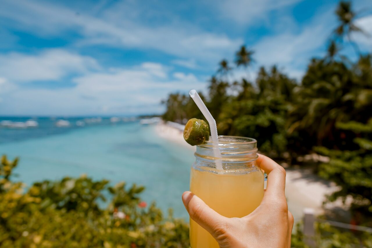 Hand holding a drink in front of a tropical beach
