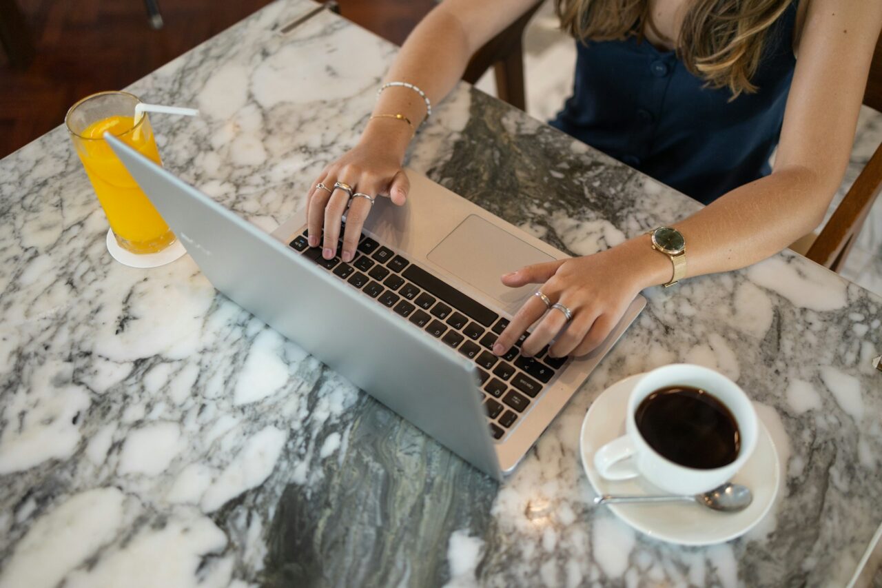 Woman typing on a laptop sitting at a marble table with coffee and orange juice