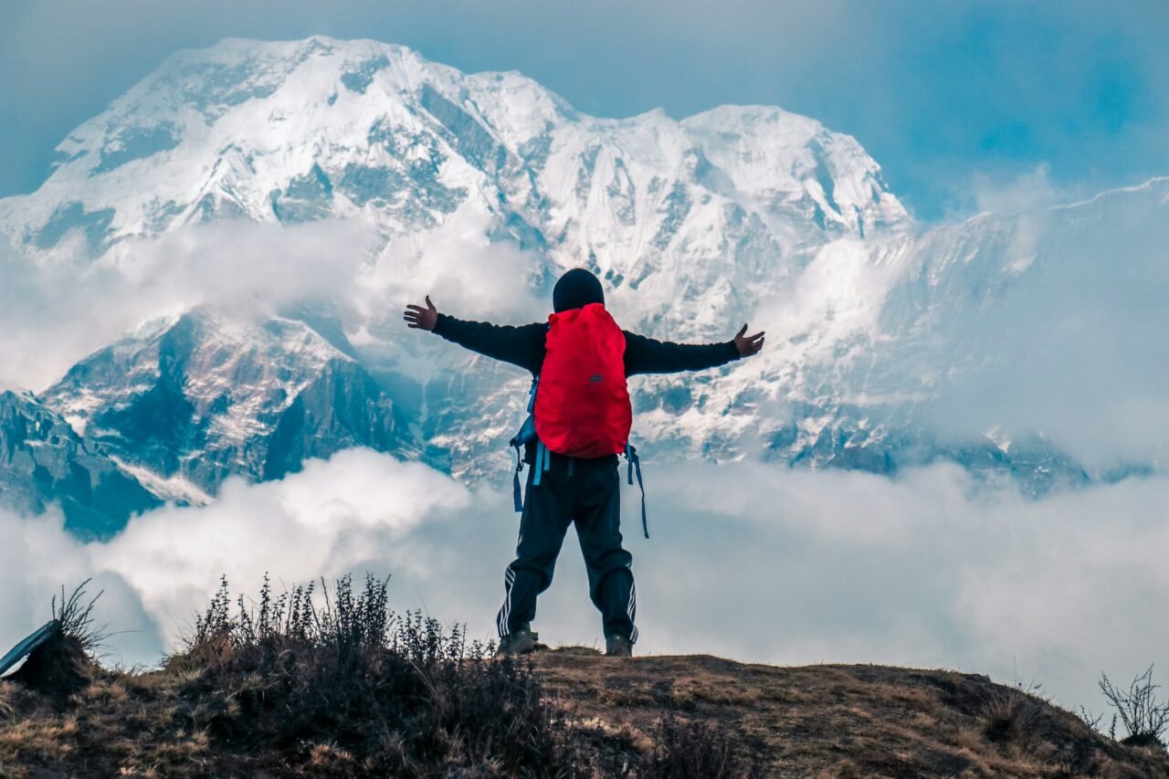 Man with red backpack standing in front of snowy mountain in Annapurna