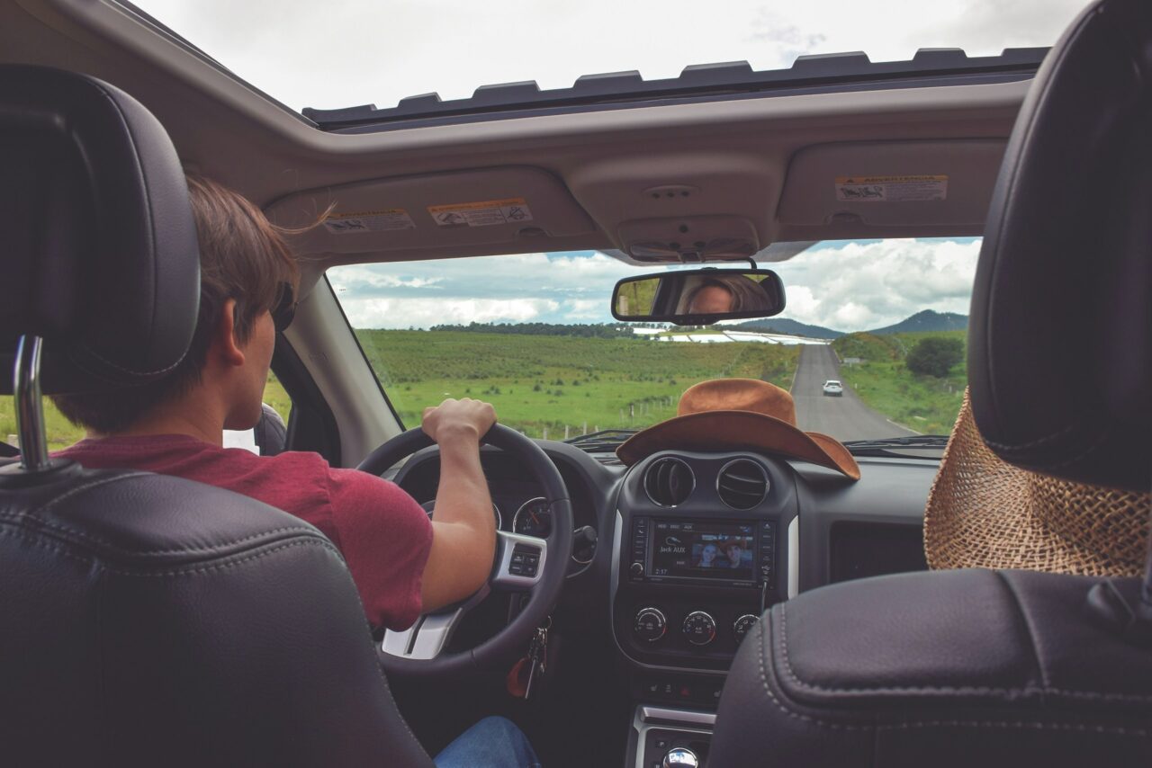Couple driving down an open road with green fields