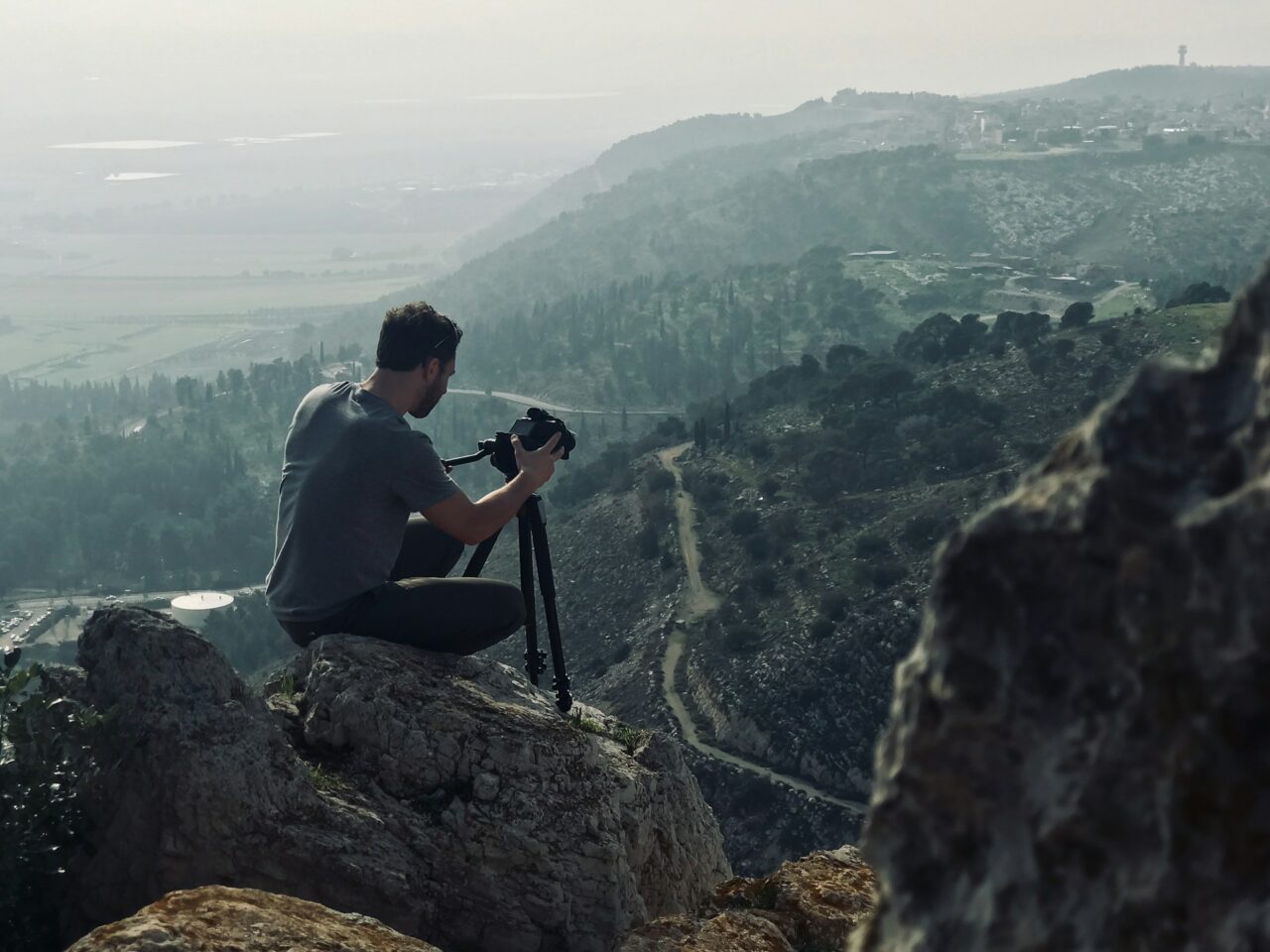 Man sitting on a mountain with a tripod and camera taking video