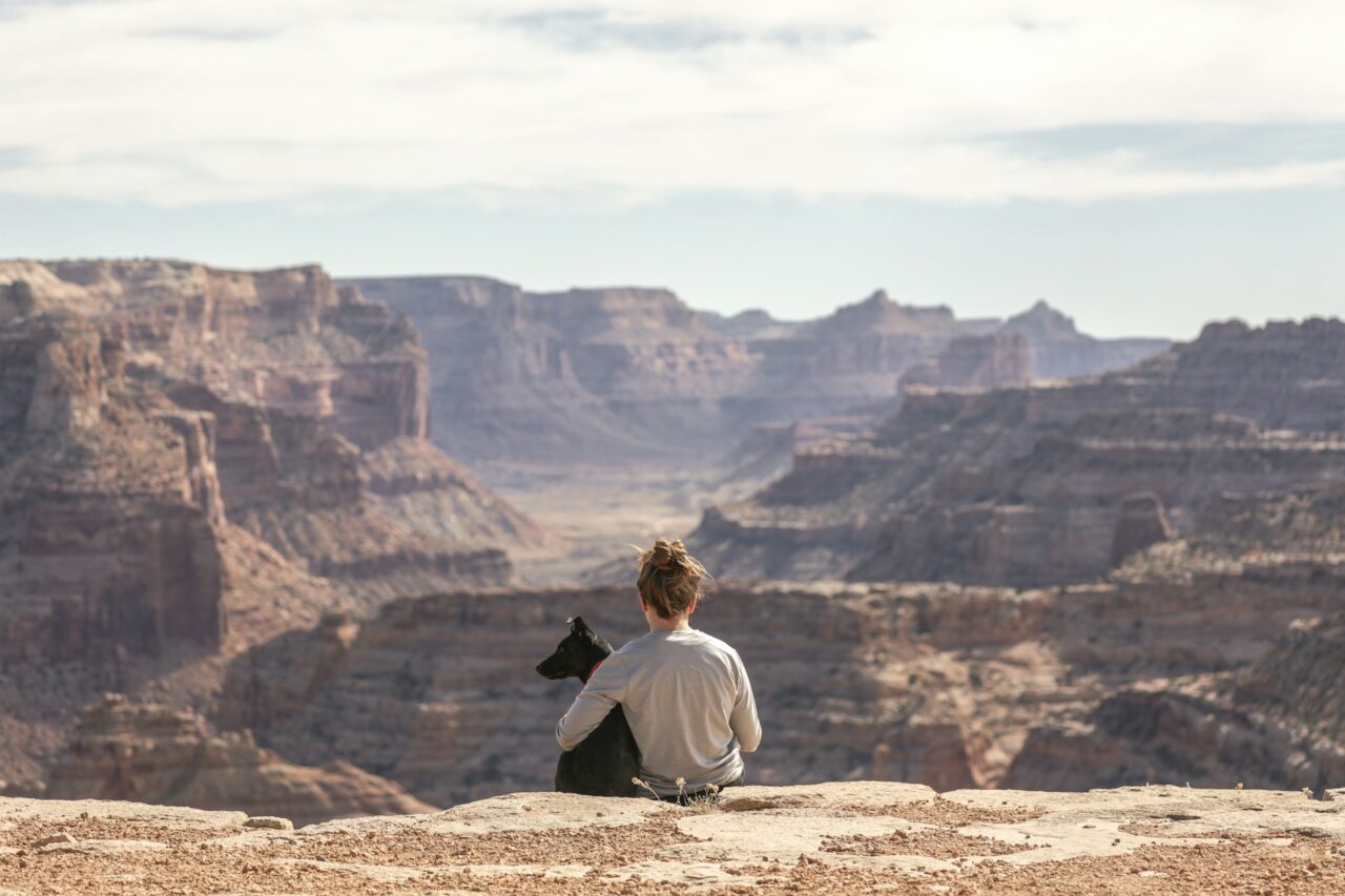 Woman with her arm around a dog sitting next to the Grand Canyon