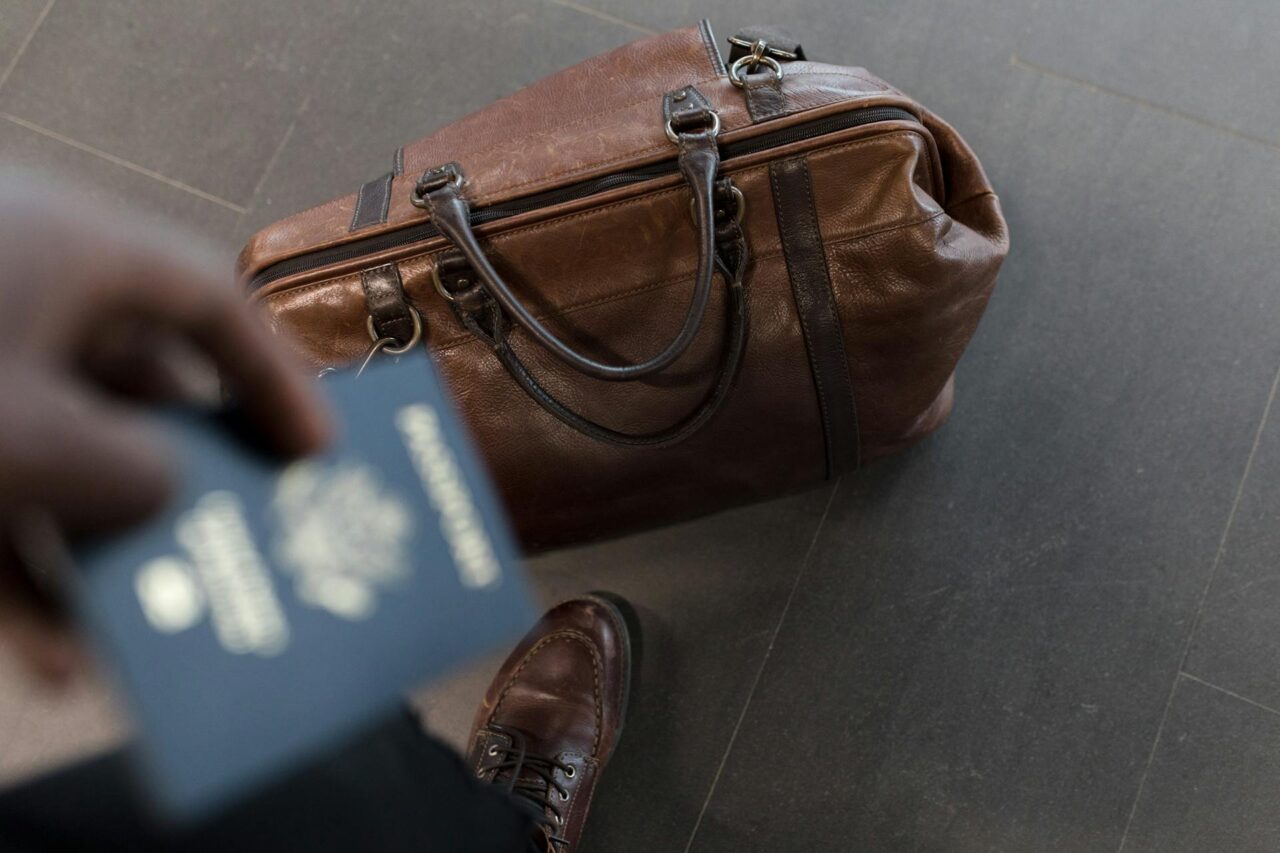 Brown duffel bag and hand holding a passport