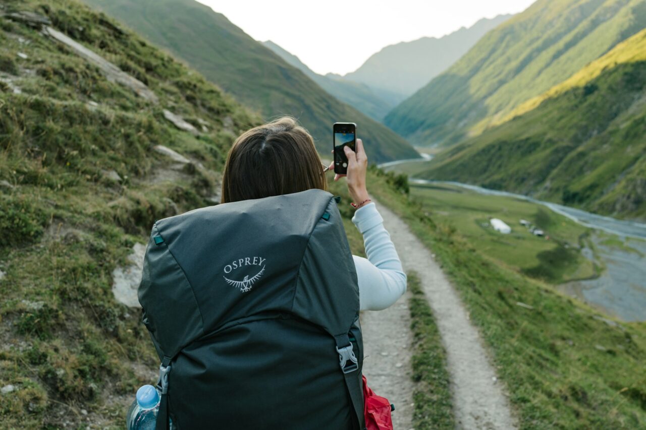 Woman with an Osprey backpack walking through mountains taking a photo