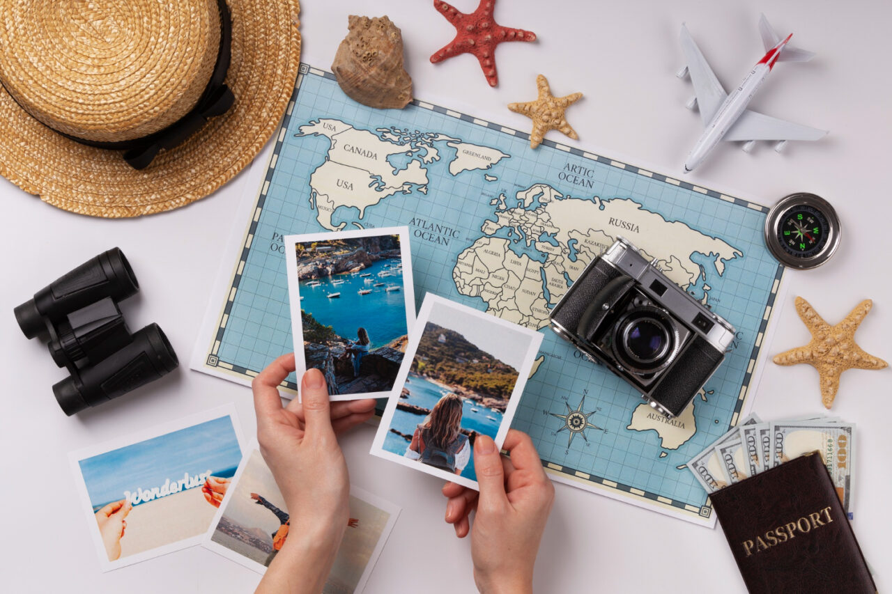 Pair of hands holding travel photos next to a map with binoculars and passport