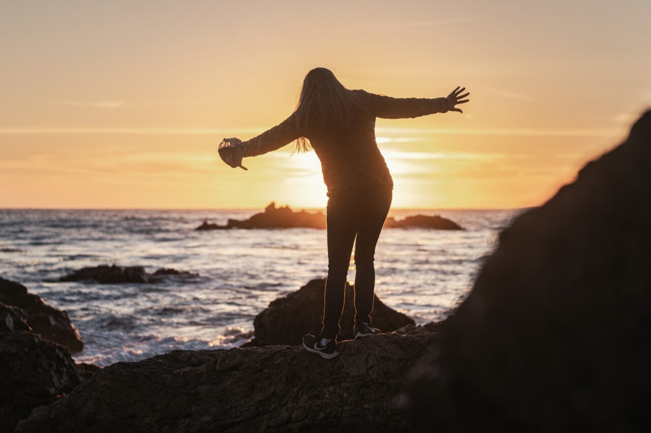 Woman standing on a rock next to the ocean trying not to slip