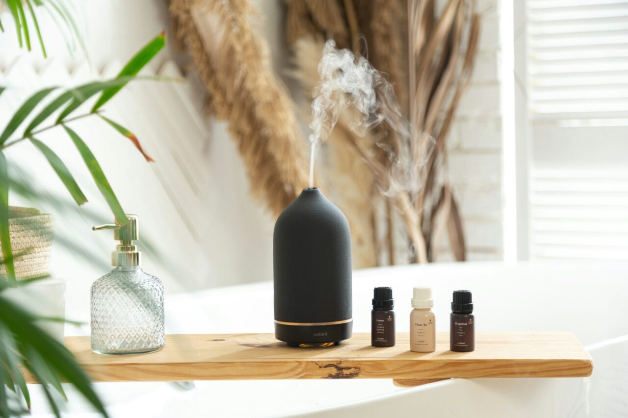 Black aromatherapy diffuser with oils on a wooden board over a bathtub