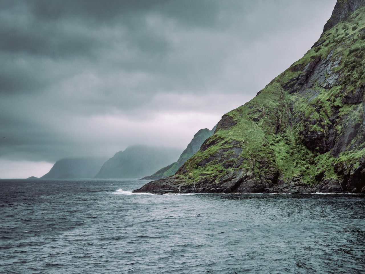 Green cliffs next to the ocean on a gloomy day in Norway