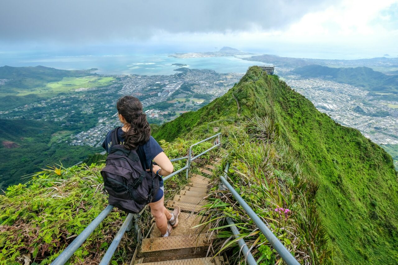 Girl with a black backpack standing on a staircase on a green mountain