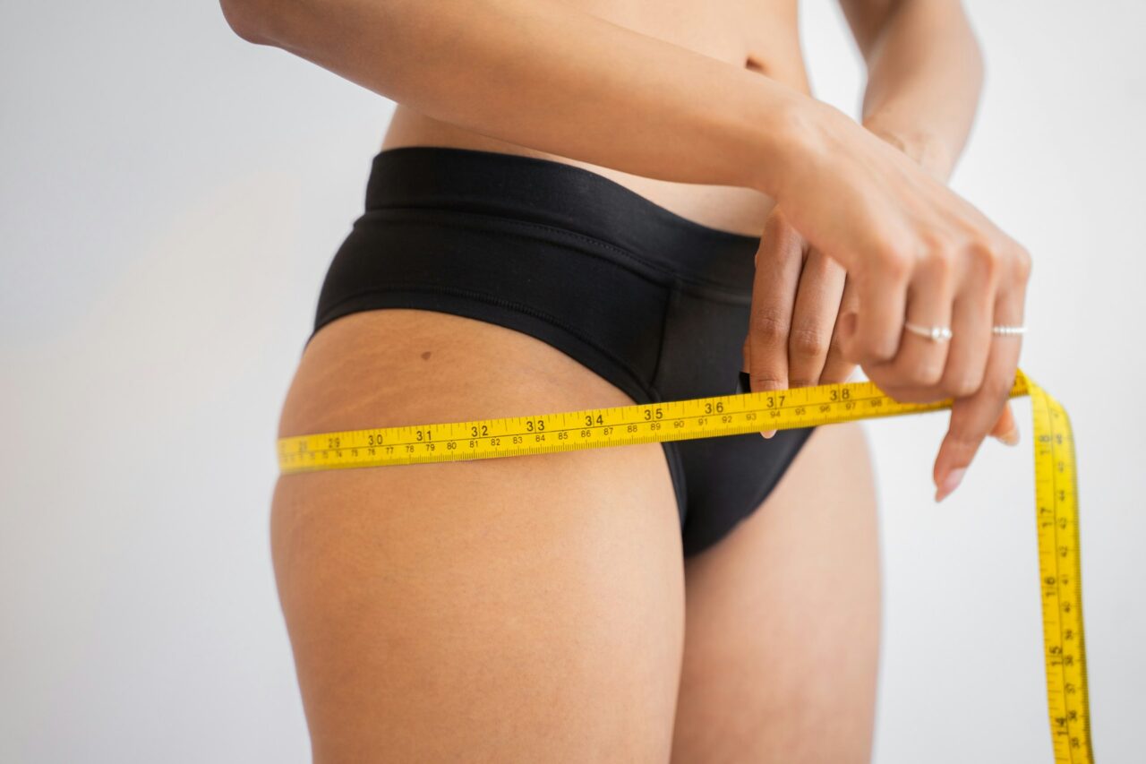 Close up of woman in black underwear with tape measure around thighs