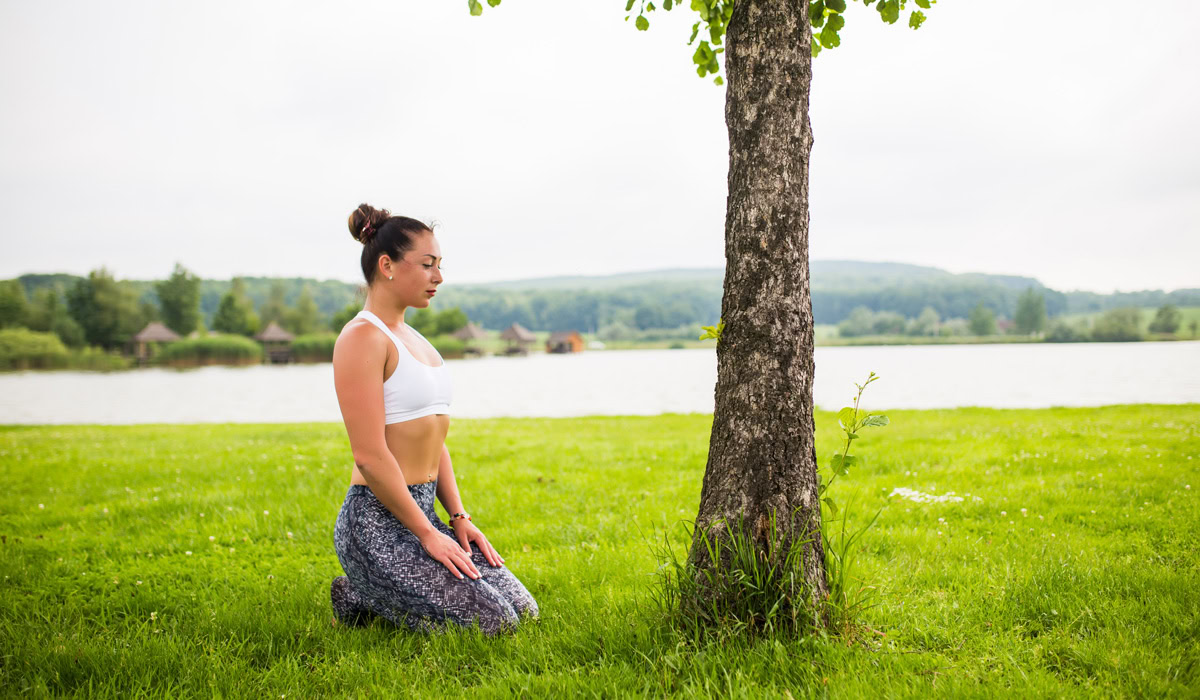 Woman meditating by tree near lake