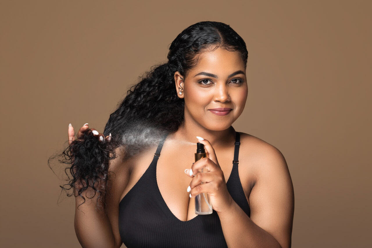 Woman with black curly hair spraying a bottle of spray