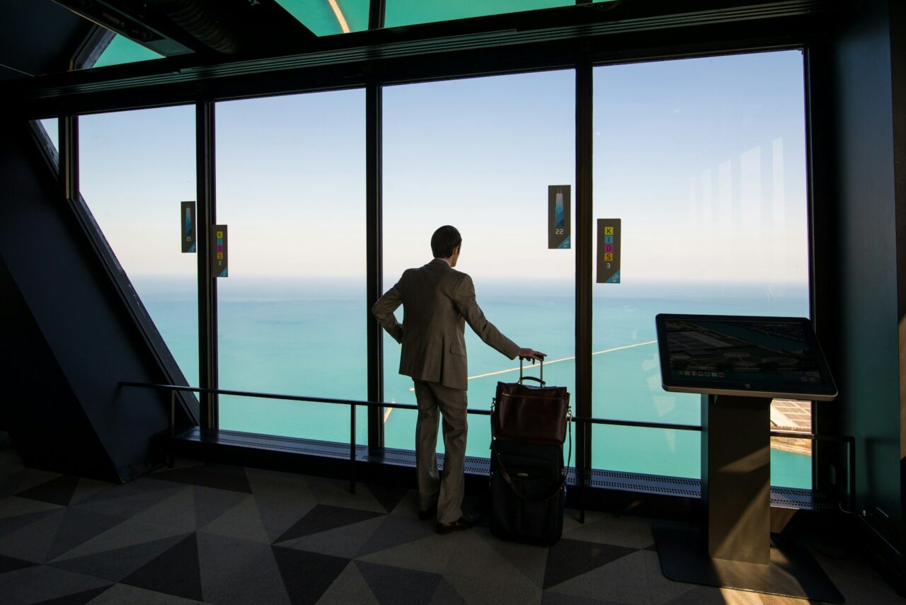 Man in suit with suitcase looking out of an airport window