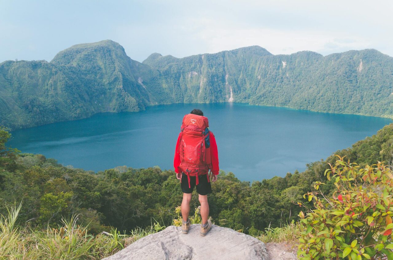 Man with red backpack looking at a lake