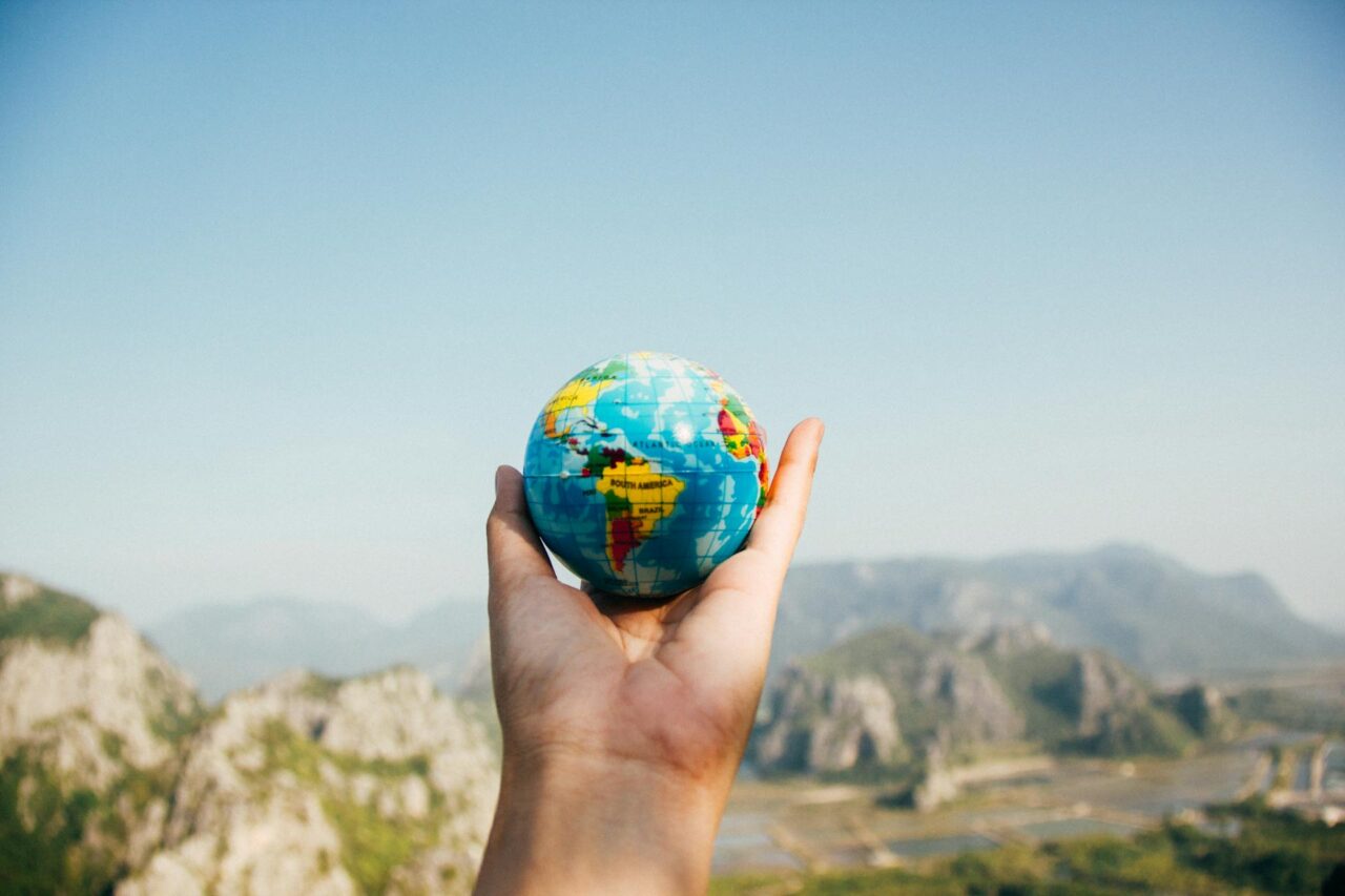Hand holding a mini globe facing a mountain