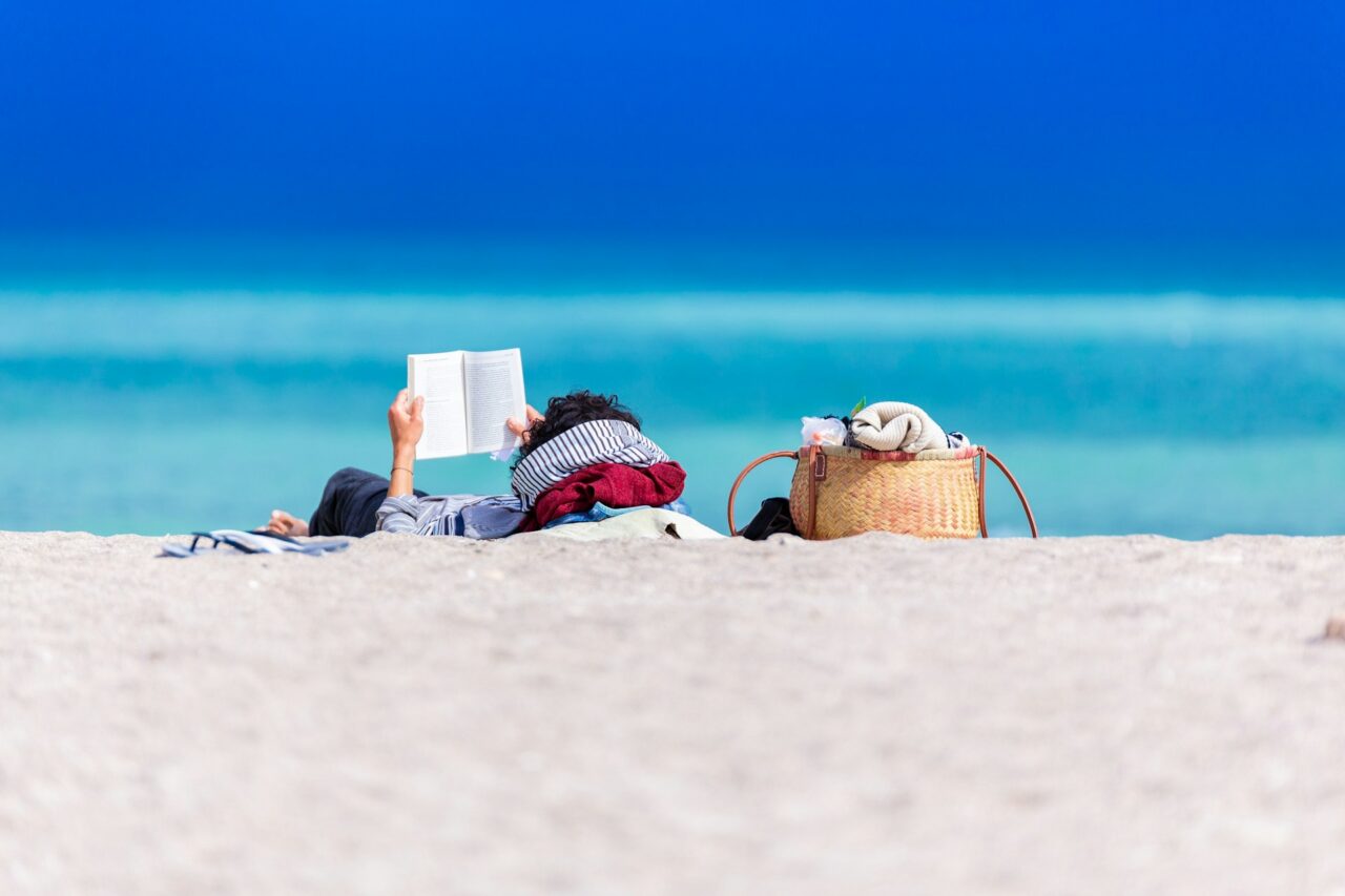Person laying down reading a book on the beach