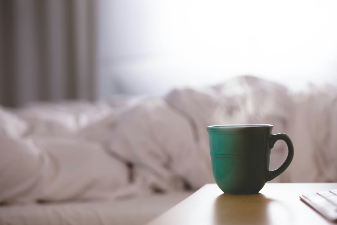 Green coffee cup next to a bed