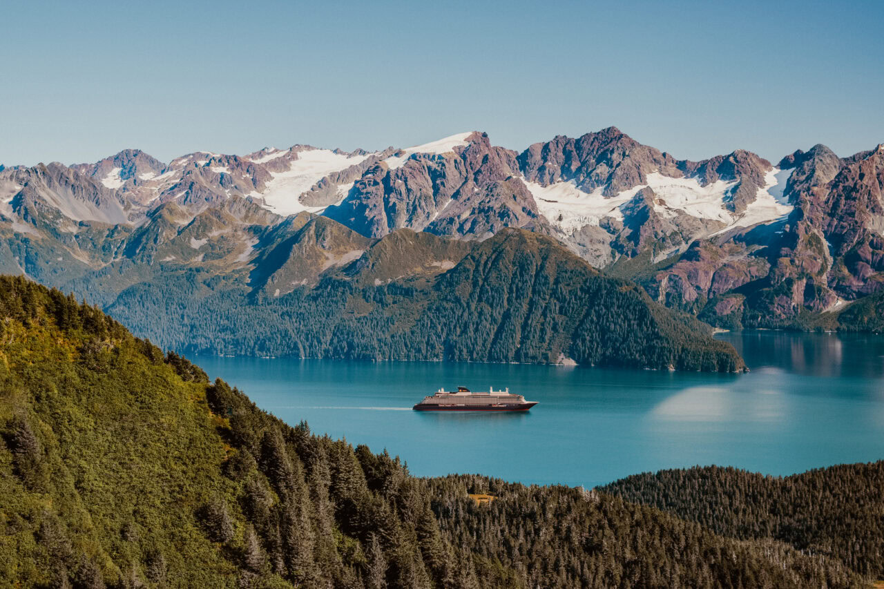 Ship traveling along a fjord with snowy mountains in the background in Alaska