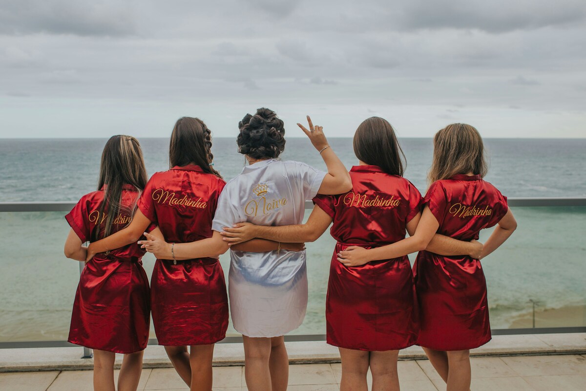 Bride and bridesmaids in robes facing the ocean on a bachelorette trip