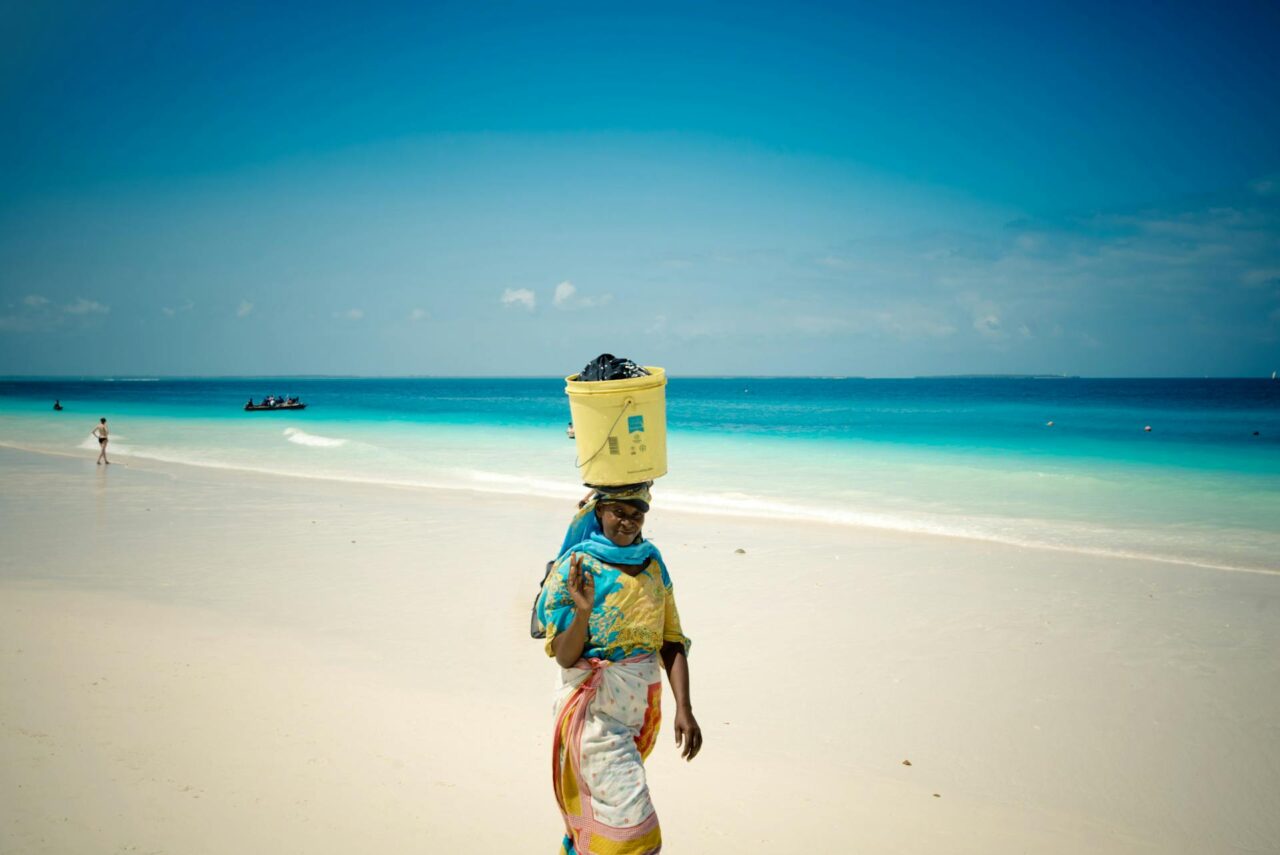 Woman walking on the beach with a bucket on her head