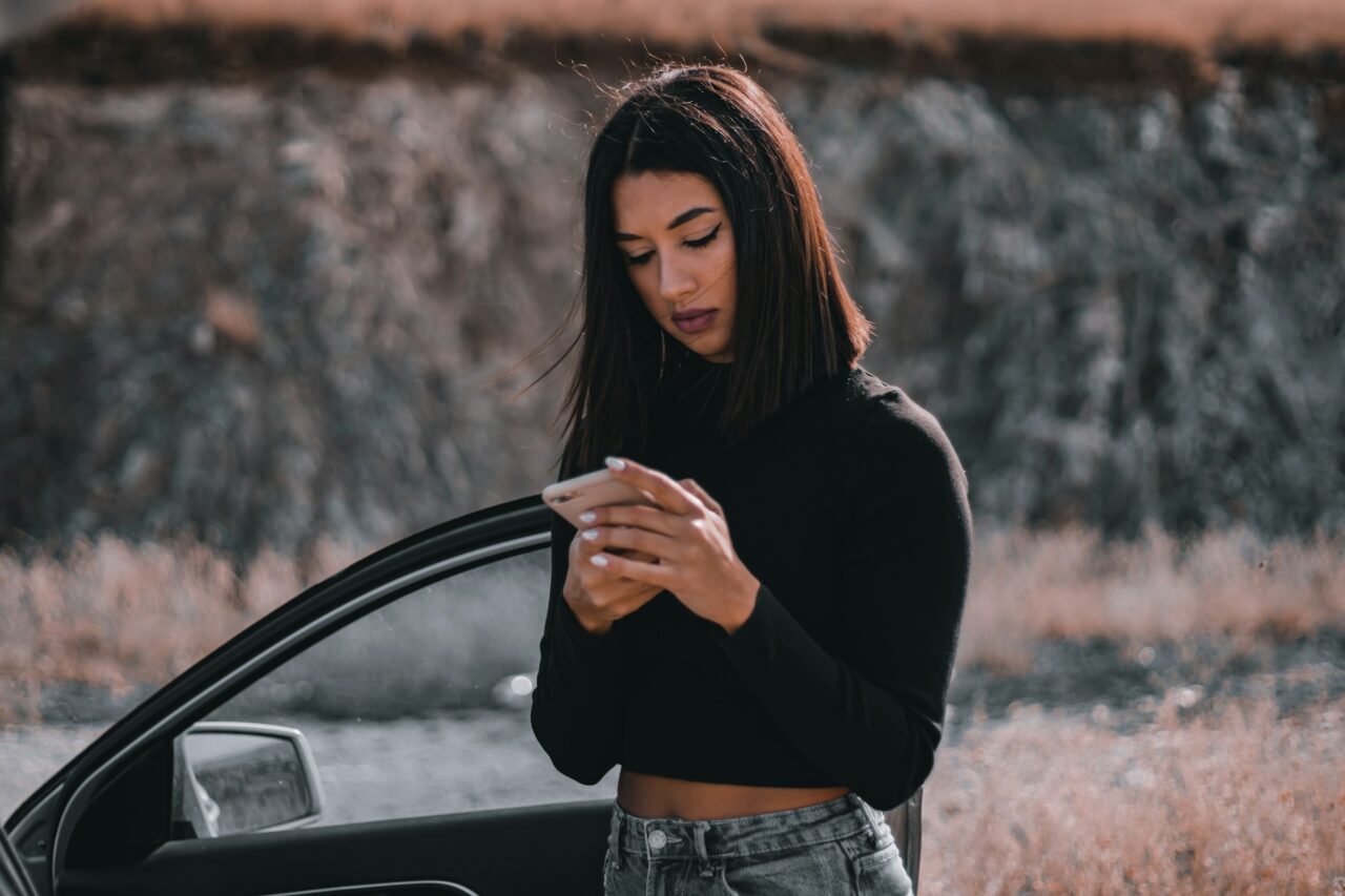 Woman standing next to a car holding a smartphone