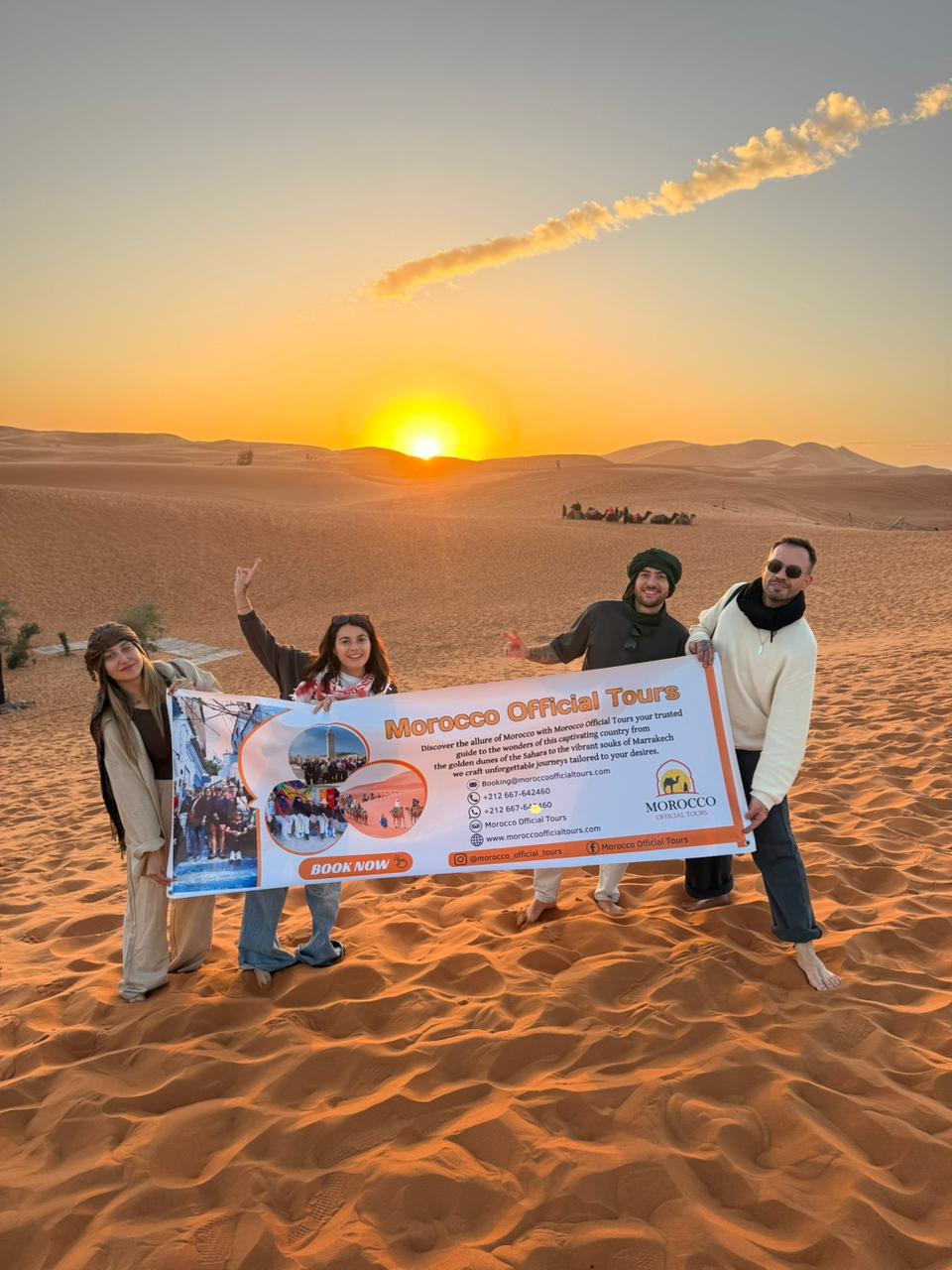 People holding a Morocco Official Tours sign in the desert