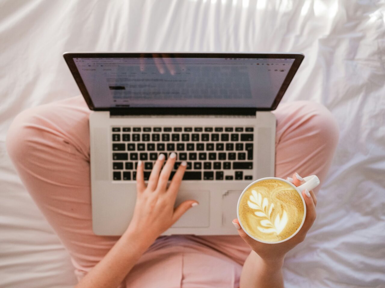 Woman sitting on a bed with laptop and coffee